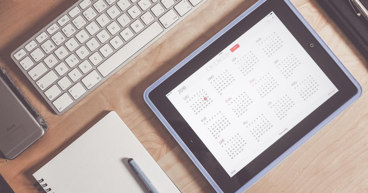 Symbolfoto zum Artikel über Multiprojektmanagement mit KI: Tablet mit Jahreskalender neben Tastatur und Notizblock auf einem Holztisch